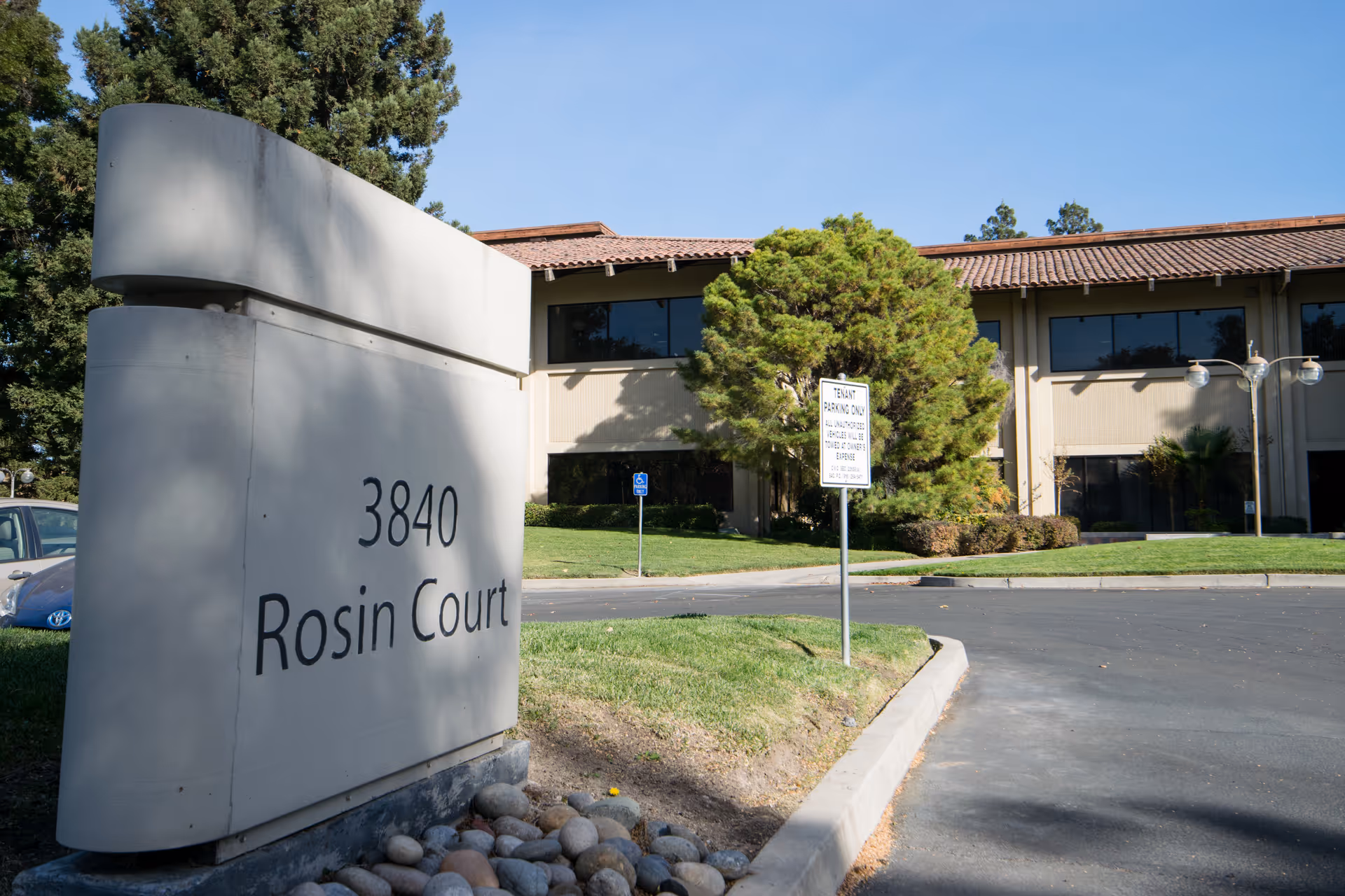 A curved concrete sign reads 3840 Rosin Court in front of a beige, two-story building.