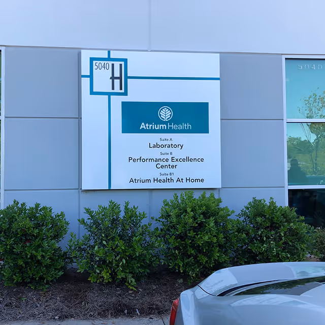 Exterior wall sign for Atrium Health At Home with shrubs and a car.
