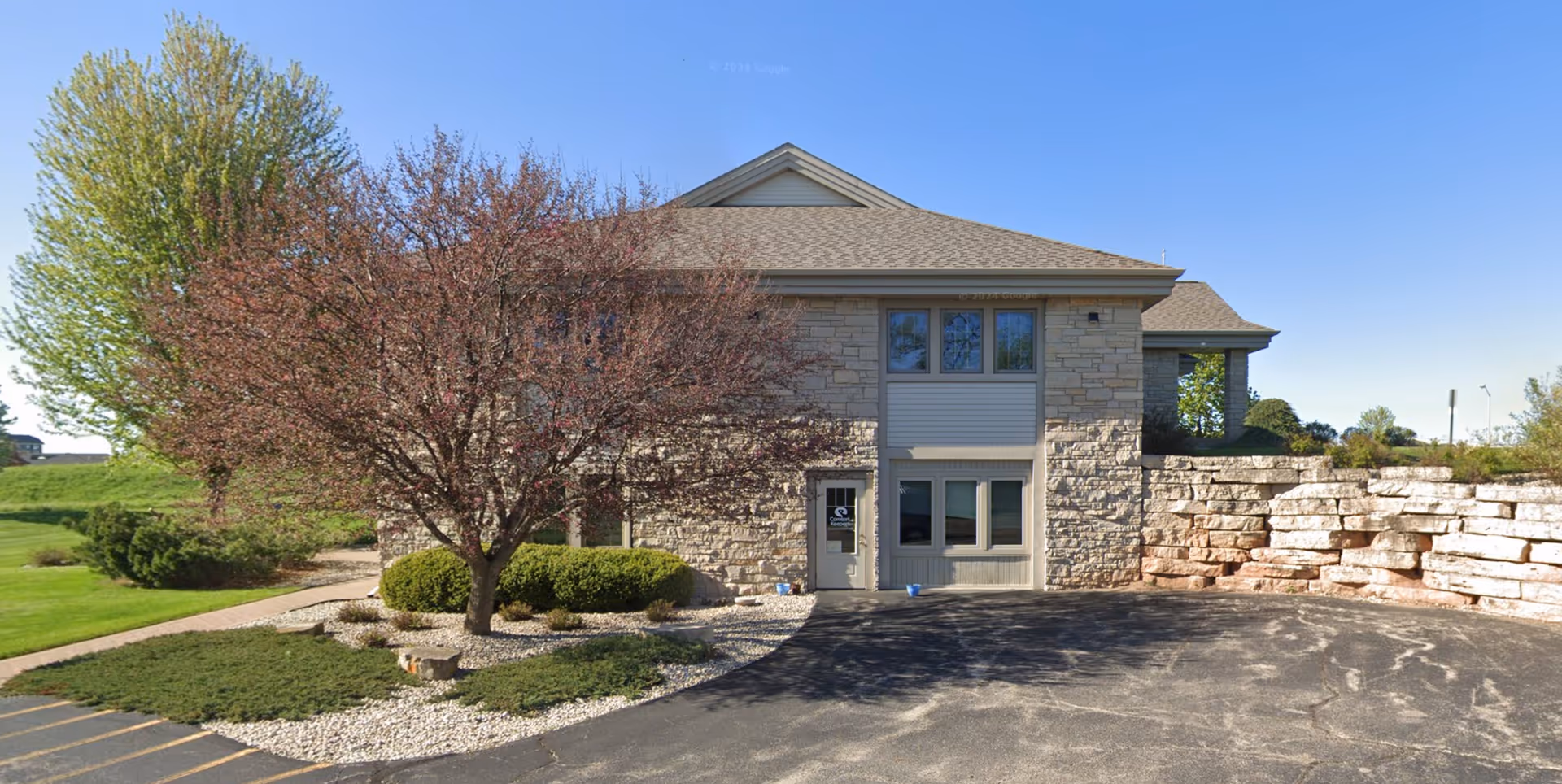 Exterior view of a stone senior living facility with landscaped entrance and parking.