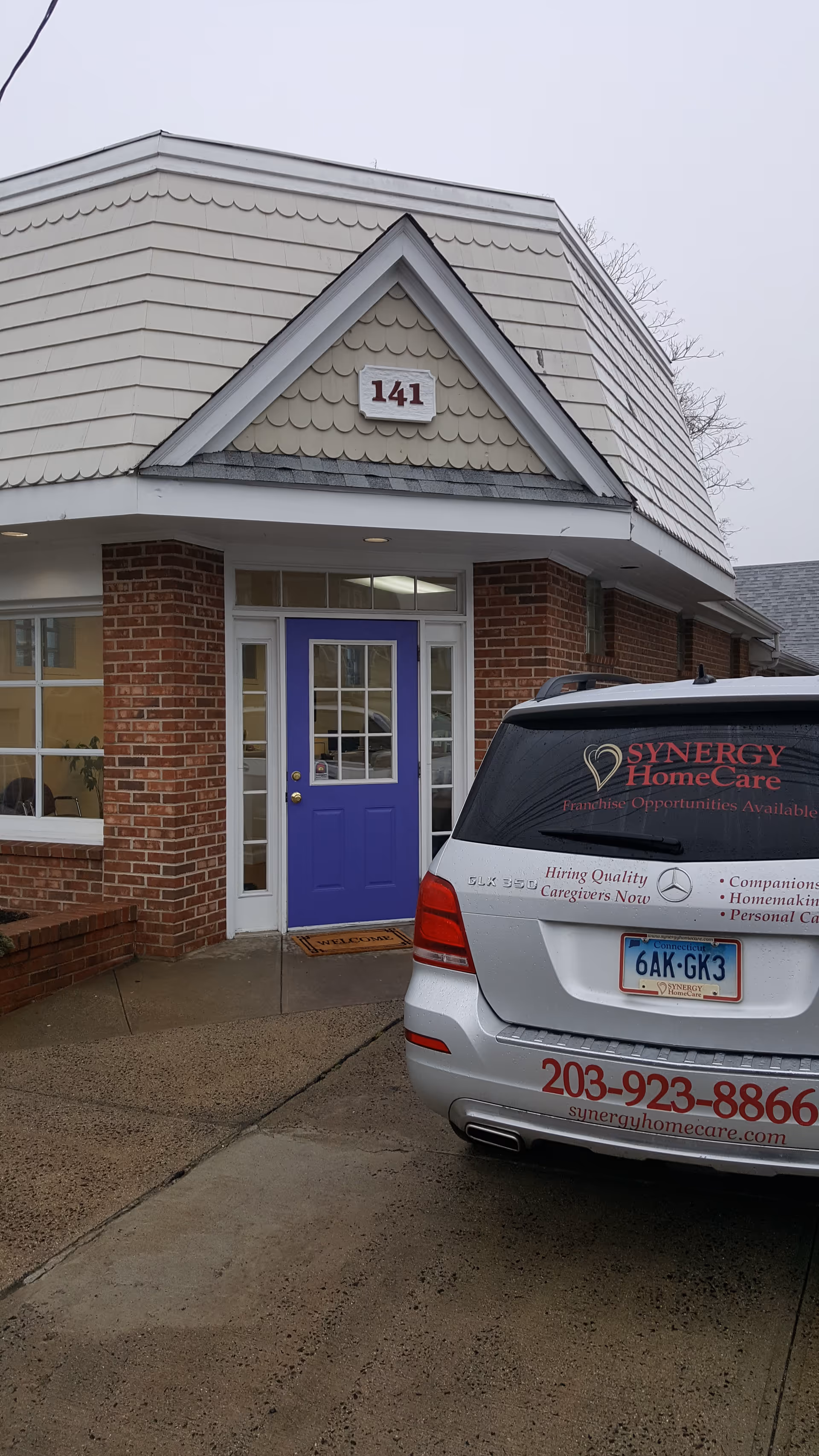 Brick exterior of a Synergy HomeCare facility with purple front door and white service van.