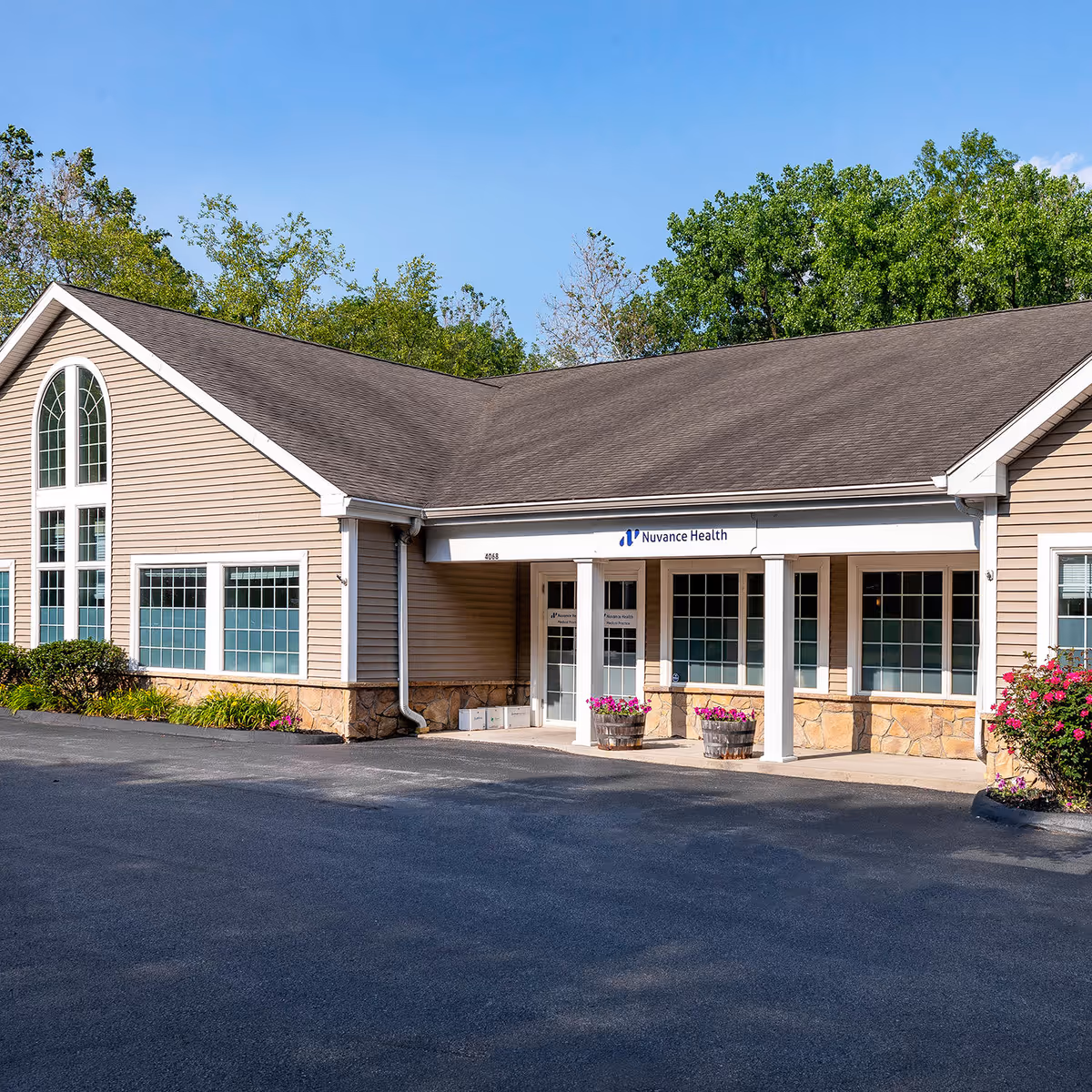 Exterior view of a beige clinic building with entrance, windows, and flower planters.