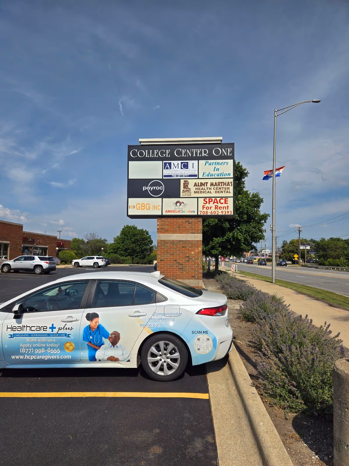 Parking lot view with College Center One sign and a Healthcare Plus Caregivers car wrap.