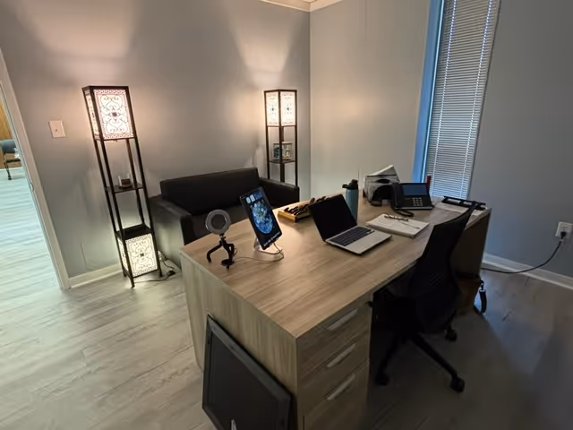 Modern home office desk with laptop, tablet, phone, and decorative floor lamps.