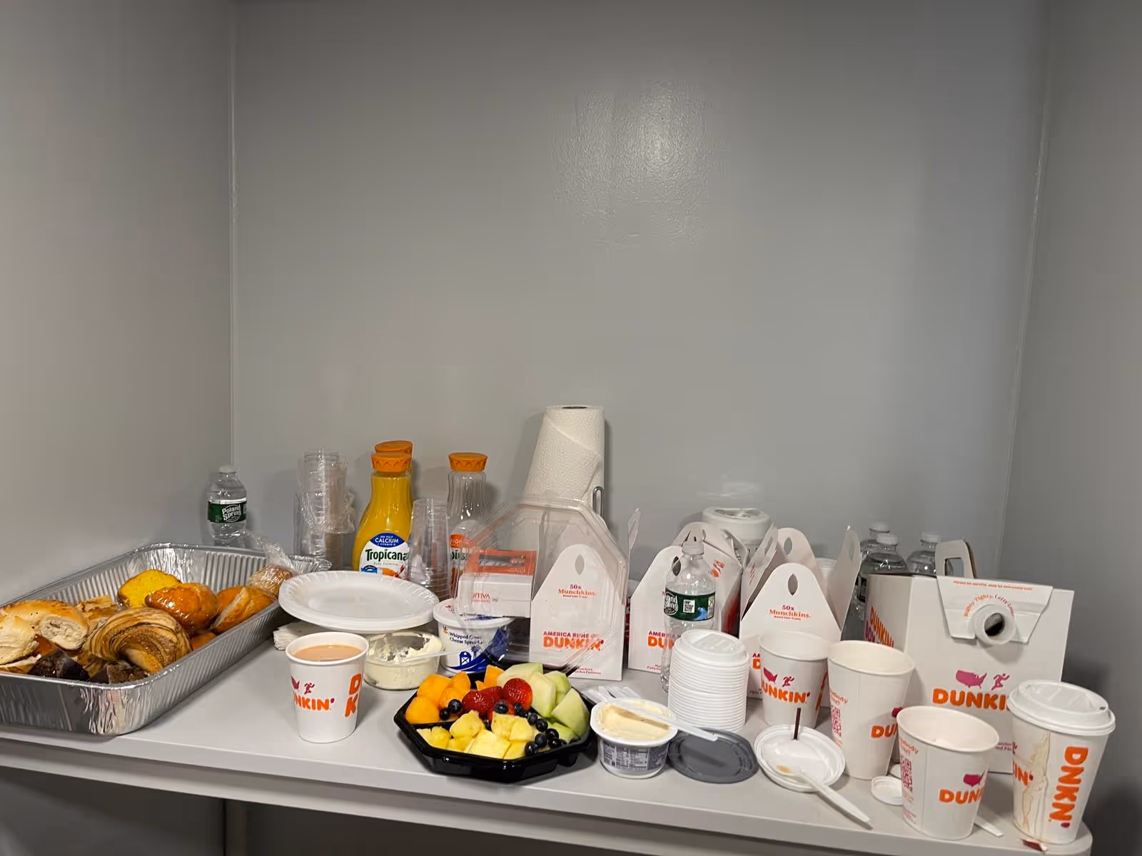 A small refreshment counter with pastries, fruit, drinks, and Dunkin cups.