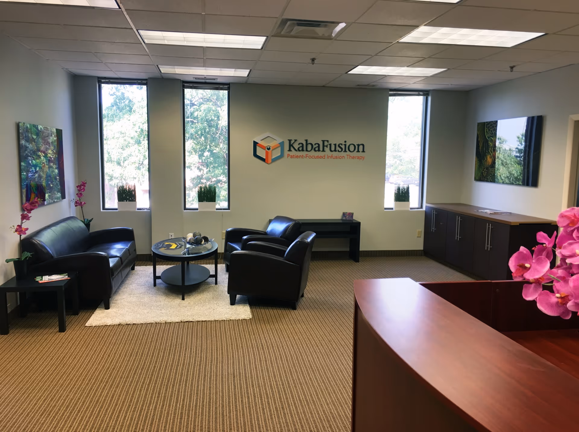 Waiting area with black leather chairs, coffee table, windows, reception desk, and KabaFusion logo on wall.