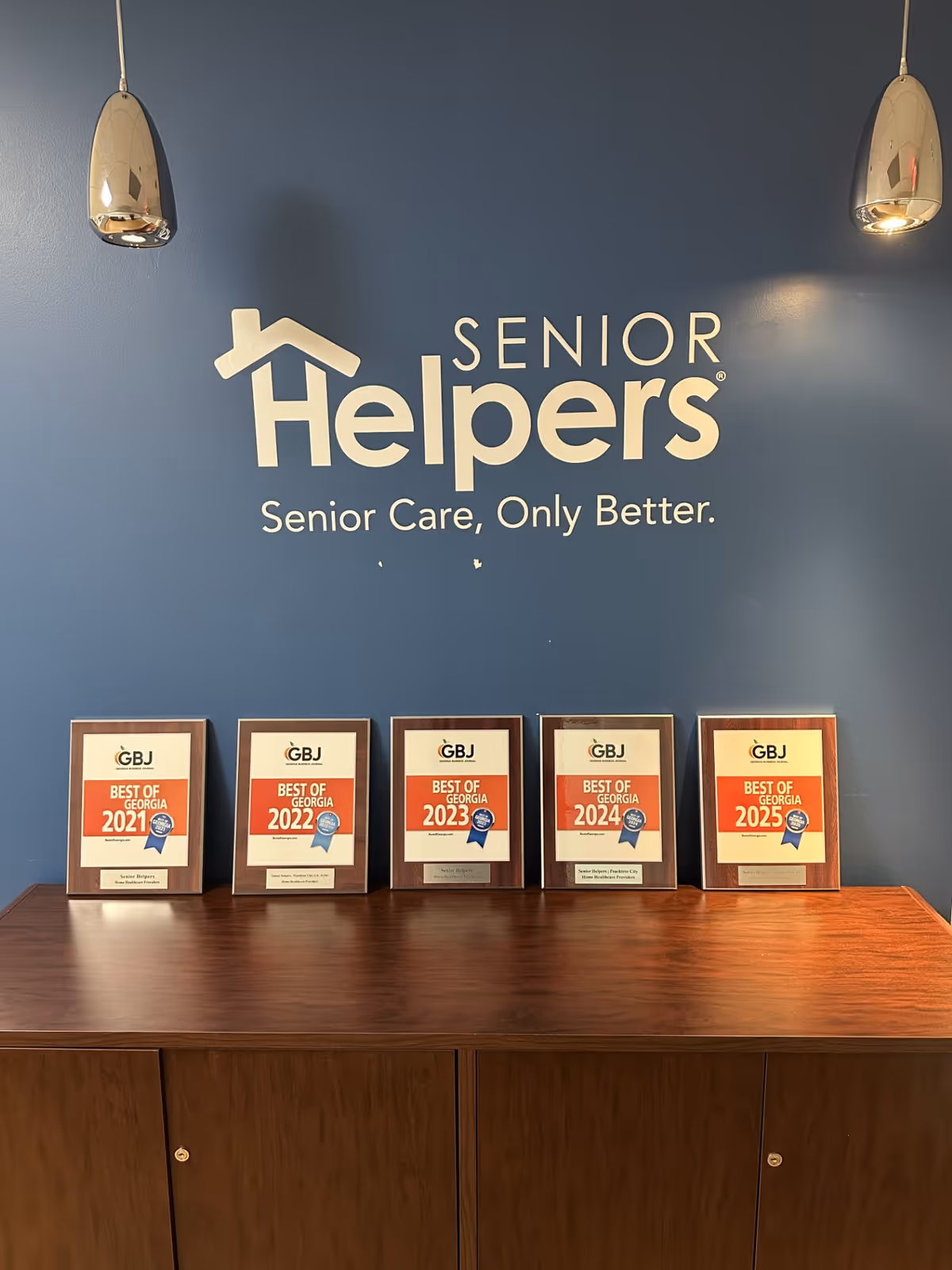 Blue wall with Senior Helpers logo and award plaques on a wooden cabinet.