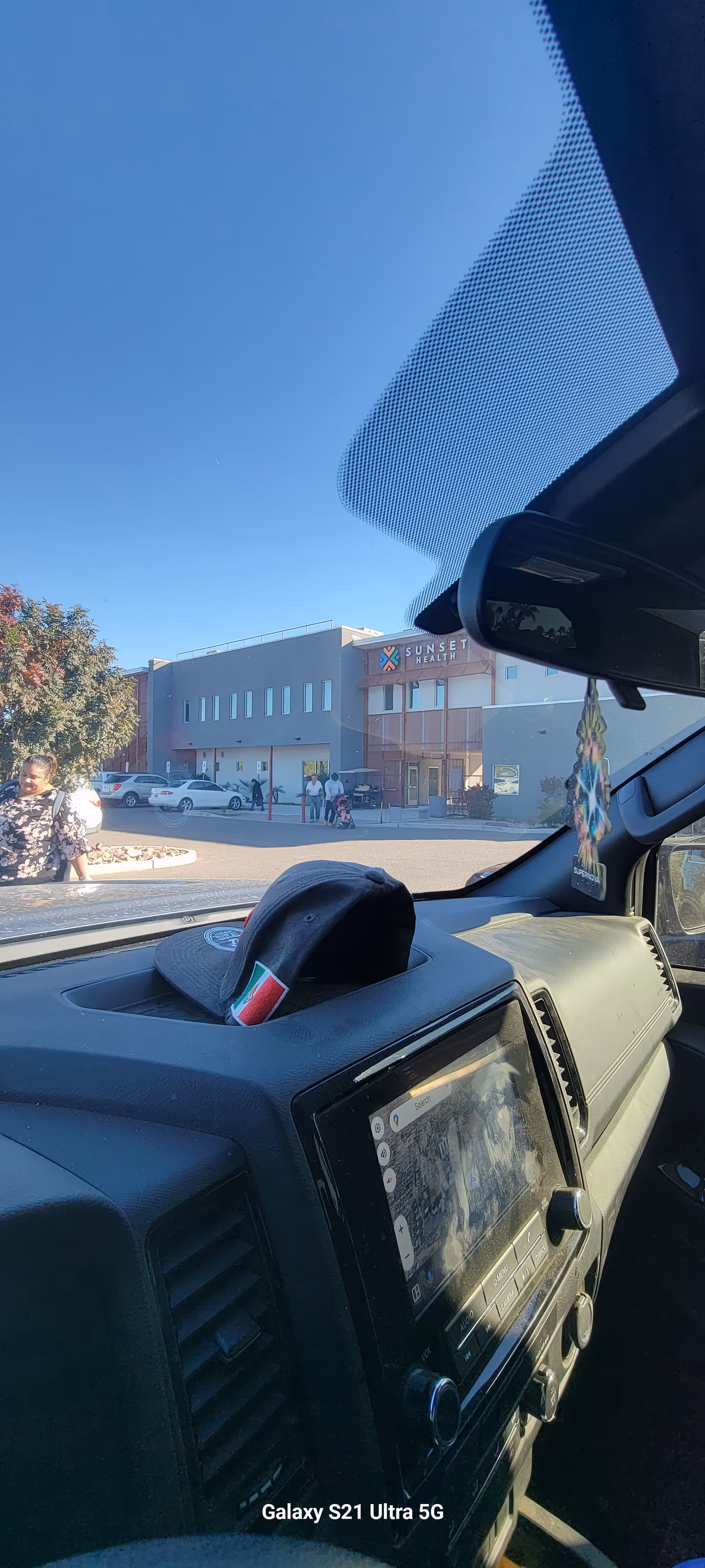 Exterior view of Sunset Health Inc facility with people near entrance and parked cars.