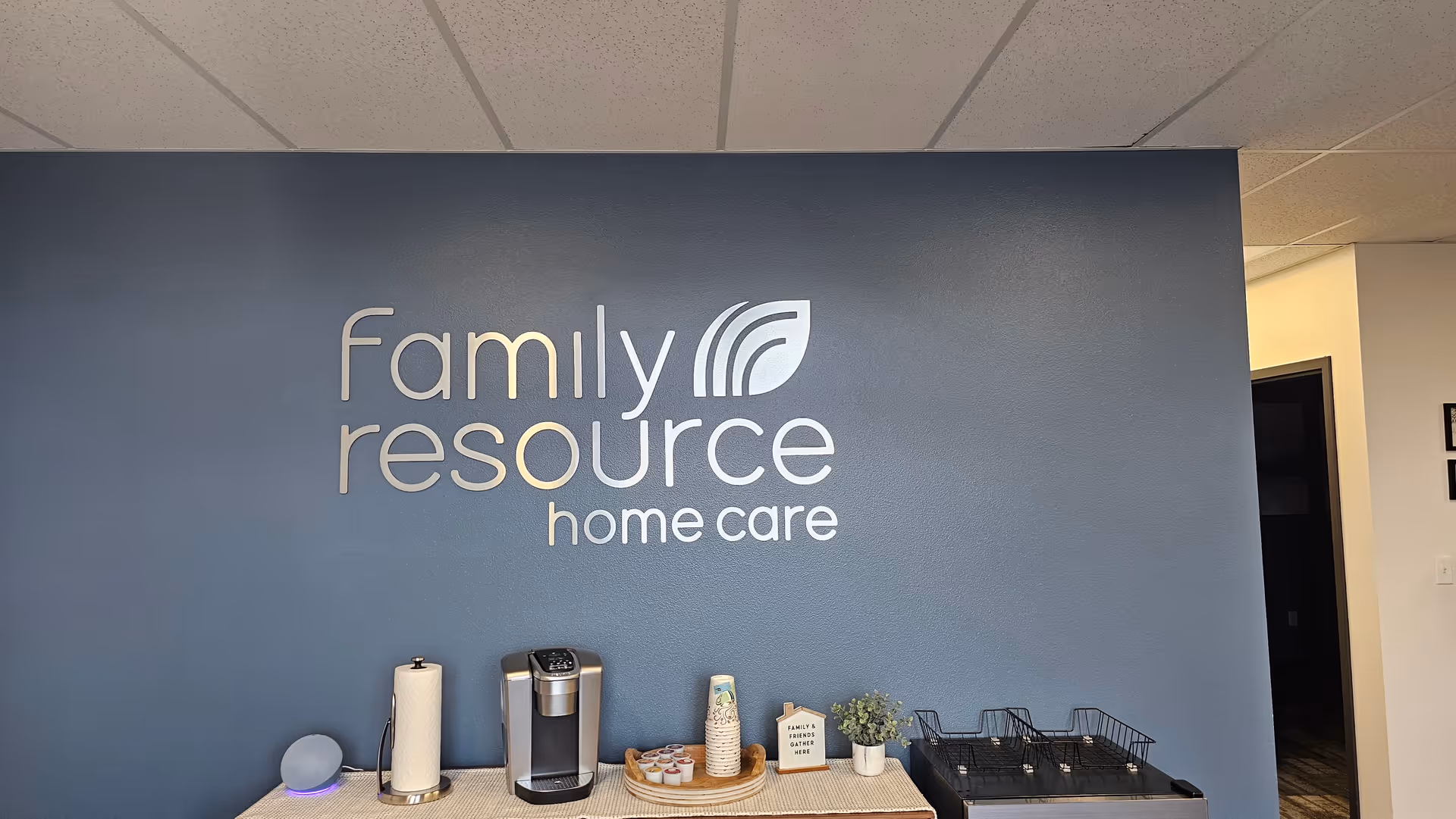 Blue interior wall features Family Resource Home Care logo; coffee station with supplies nearby.