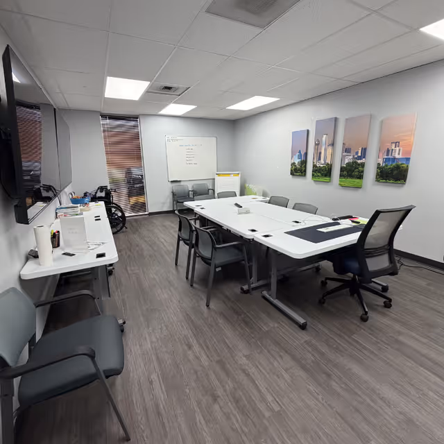 A modern conference room with tables, chairs, whiteboard, and wall art in a care facility.
