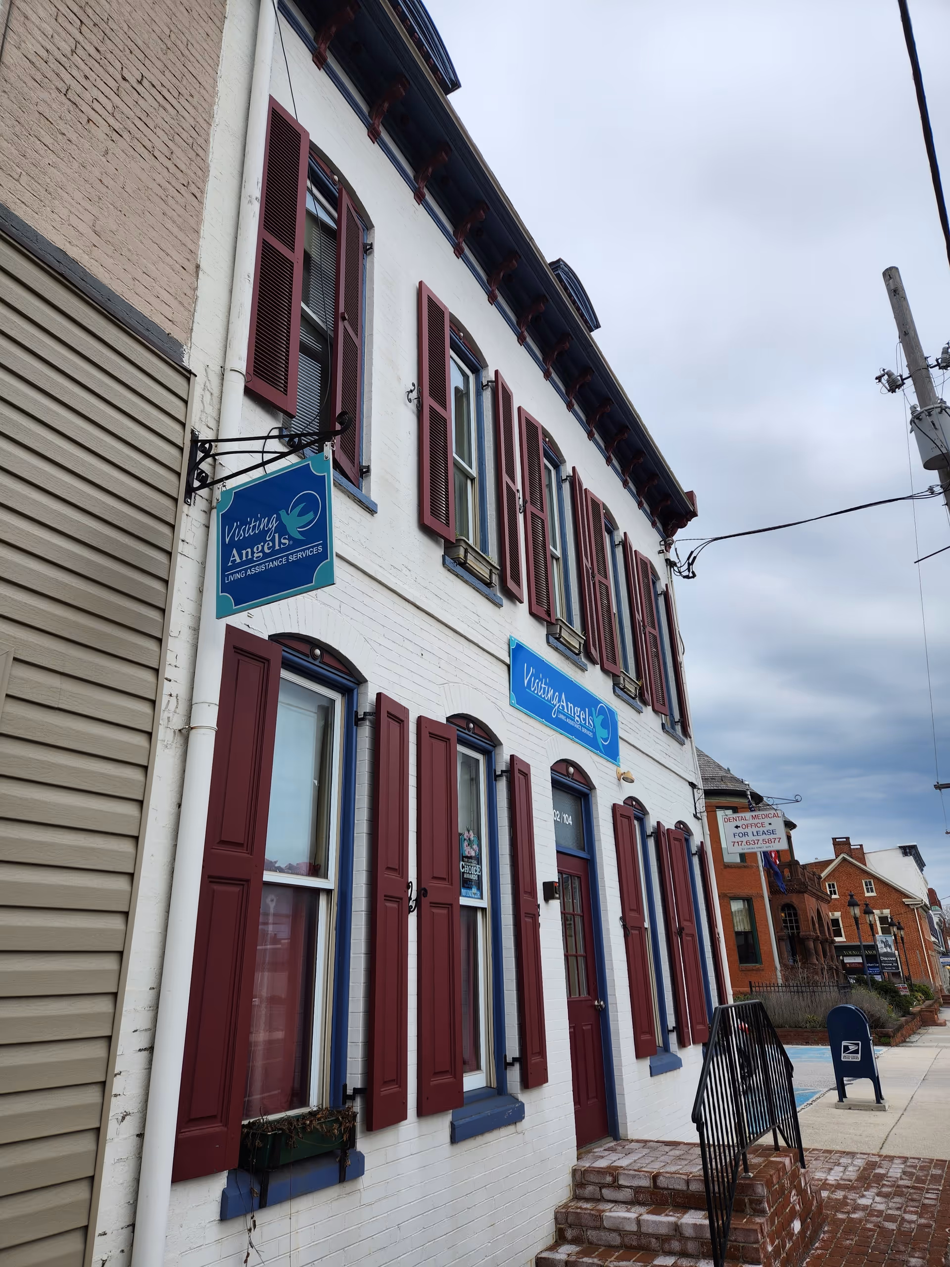 White brick building with maroon shutters and a blue Visiting Angels sign.