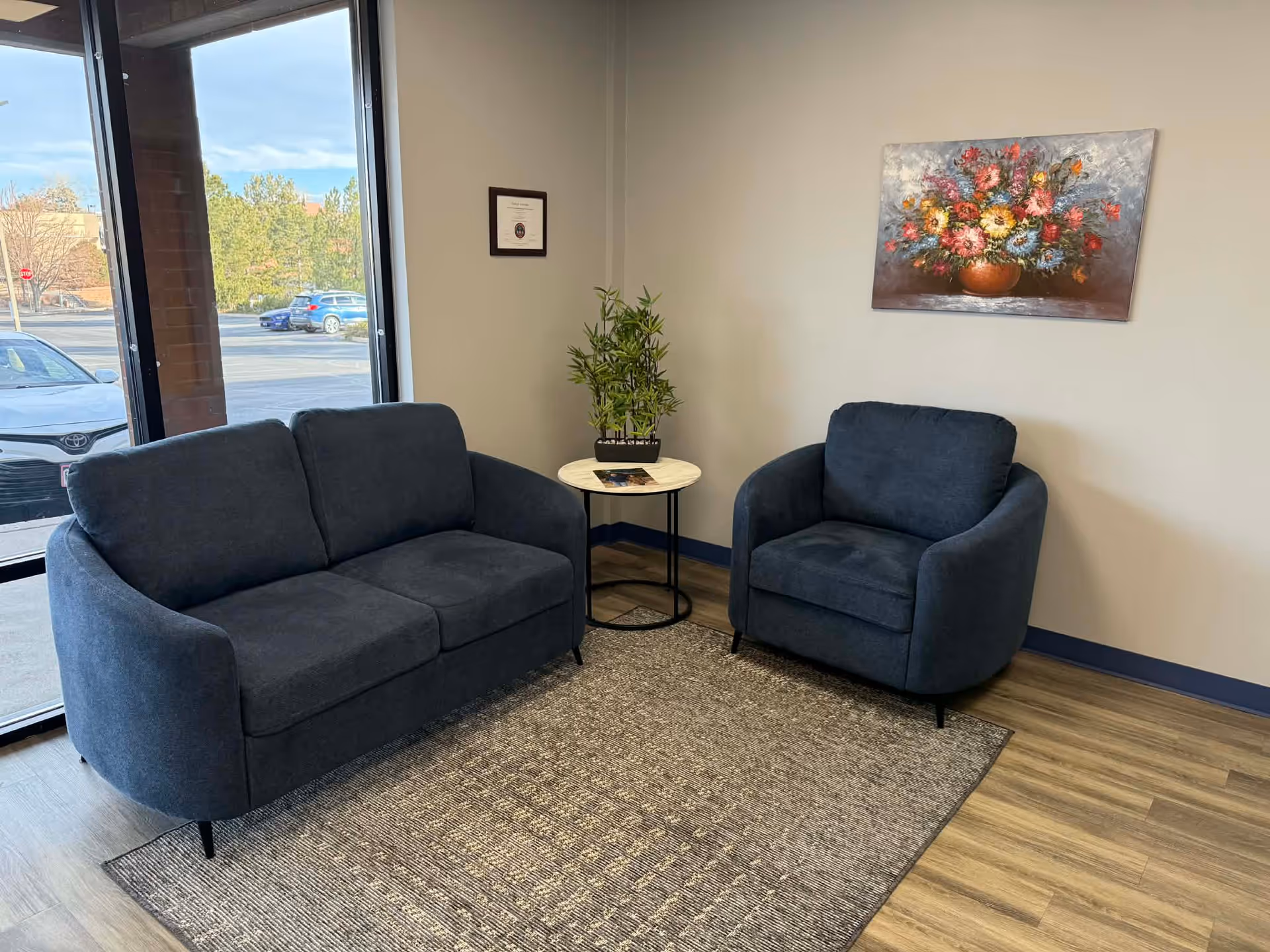 Blue sofa and chair seating area with plant, rug, and floral wall art in lobby.