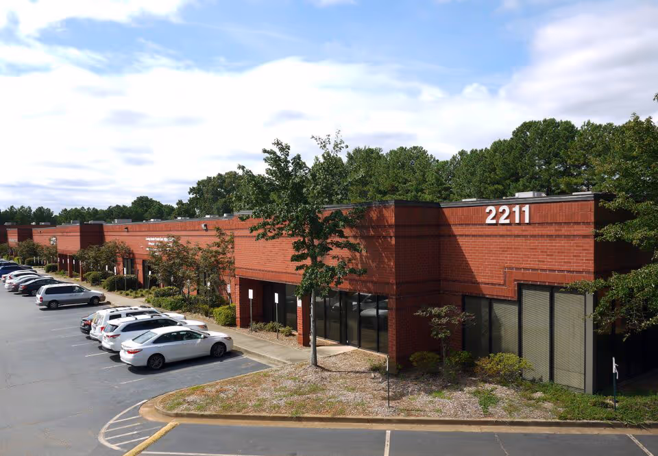 Exterior view of a brick assisted living facility with a parking lot and surrounding trees