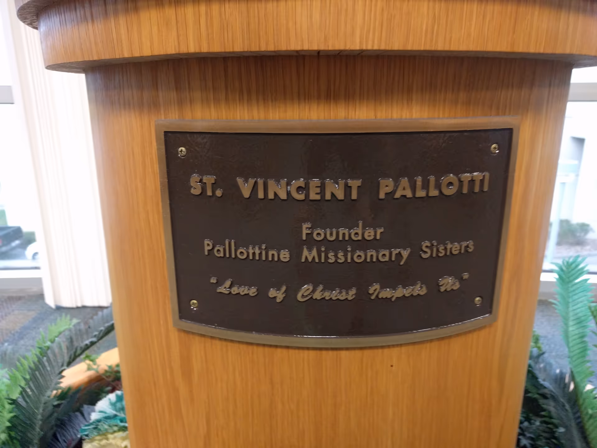 Wooden pillar with bronze plaque honoring St. Vincent Pallotti inside a facility lobby.