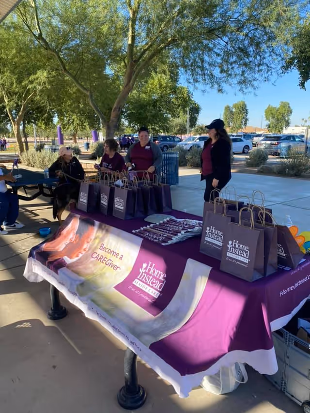 Outdoor table with Home Instead promotional bags and staff at a community event.