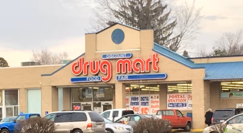 Front exterior of a Discount Drug Mart storefront with parked cars.