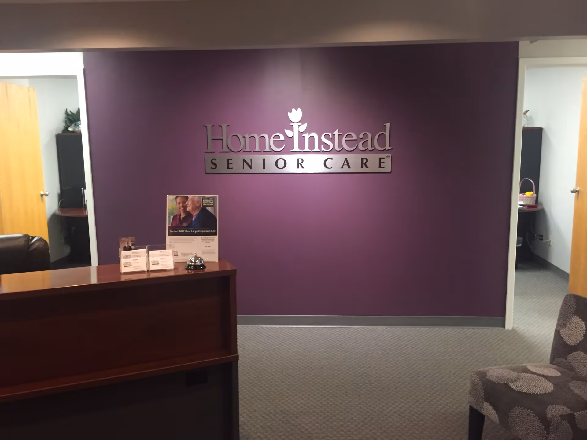 Reception desk in a purple-walled lobby with Home Instead Senior Care sign.