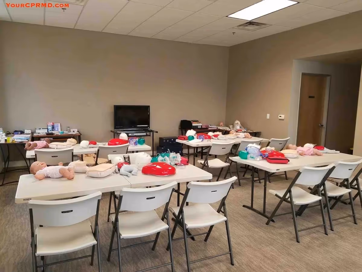 Training room with multiple tables, folding chairs, and CPR mannequins for education.