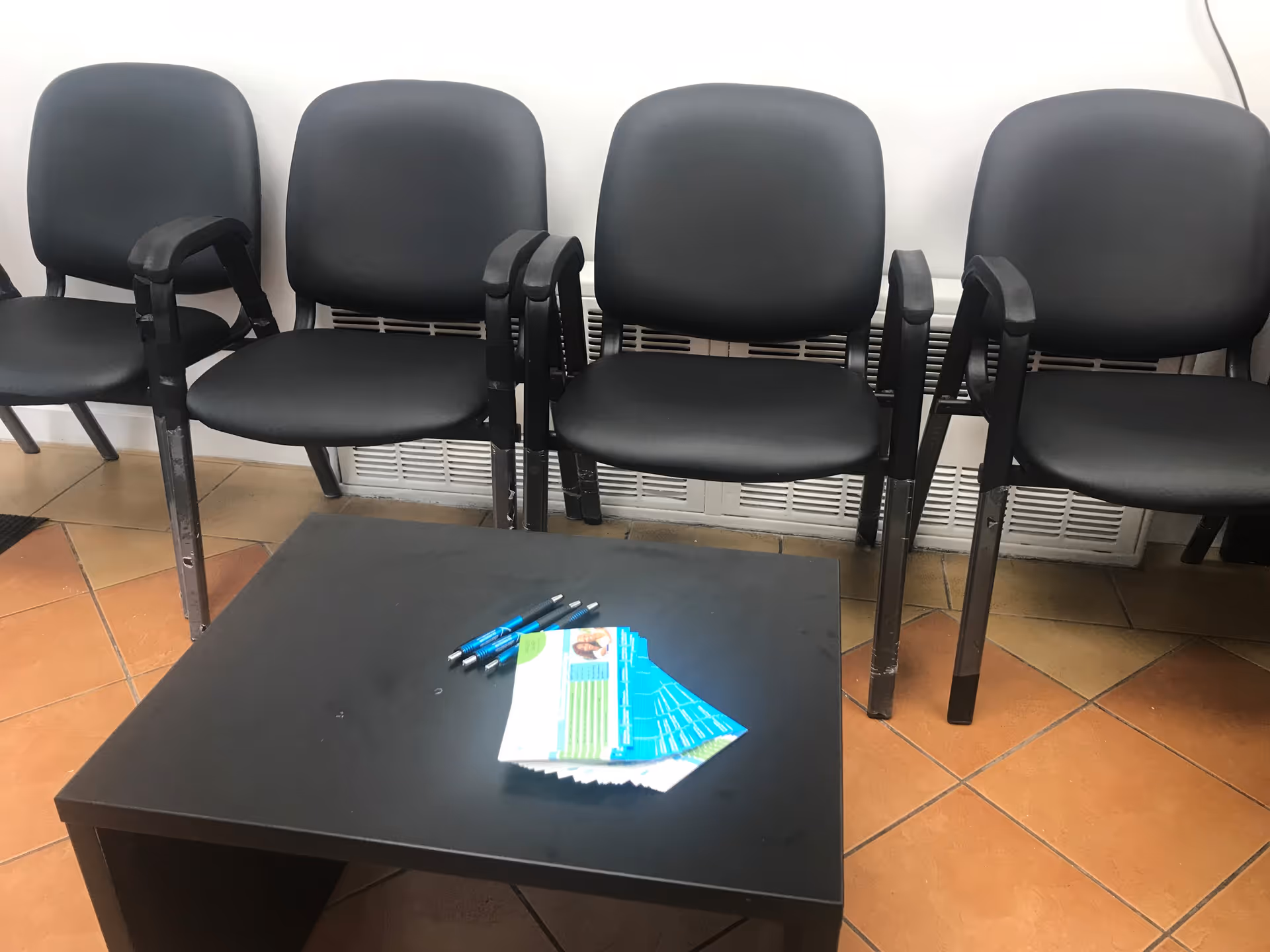 Row of black chairs along a wall with a small table and papers.