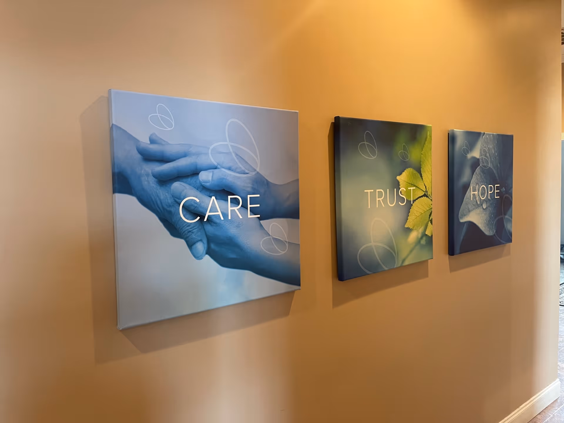 Three canvas prints reading CARE, TRUST, HOPE along a beige interior wall.