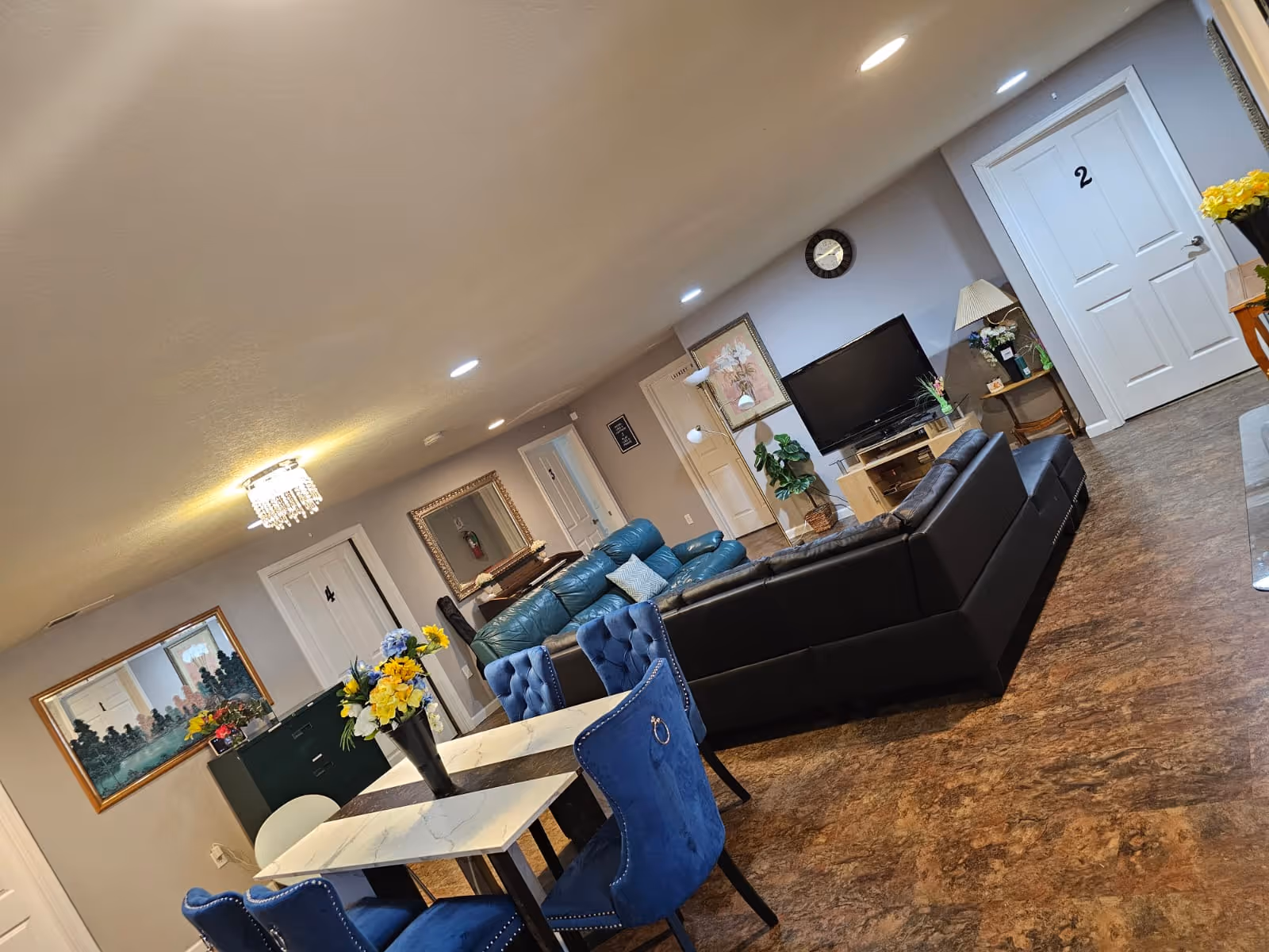 A spacious, well-lit living area features a black sectional sofa, TV, and dining table.