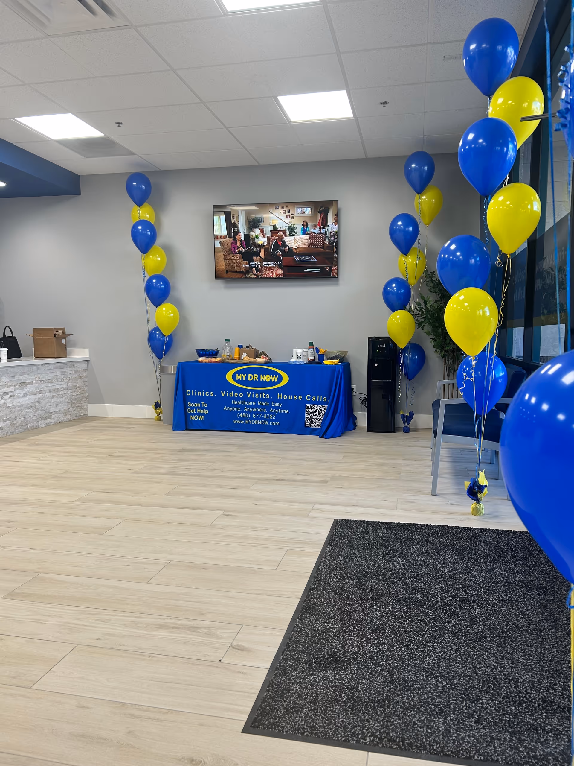 Reception area with blue and yellow balloons and a MY DR NOW info table indoors.