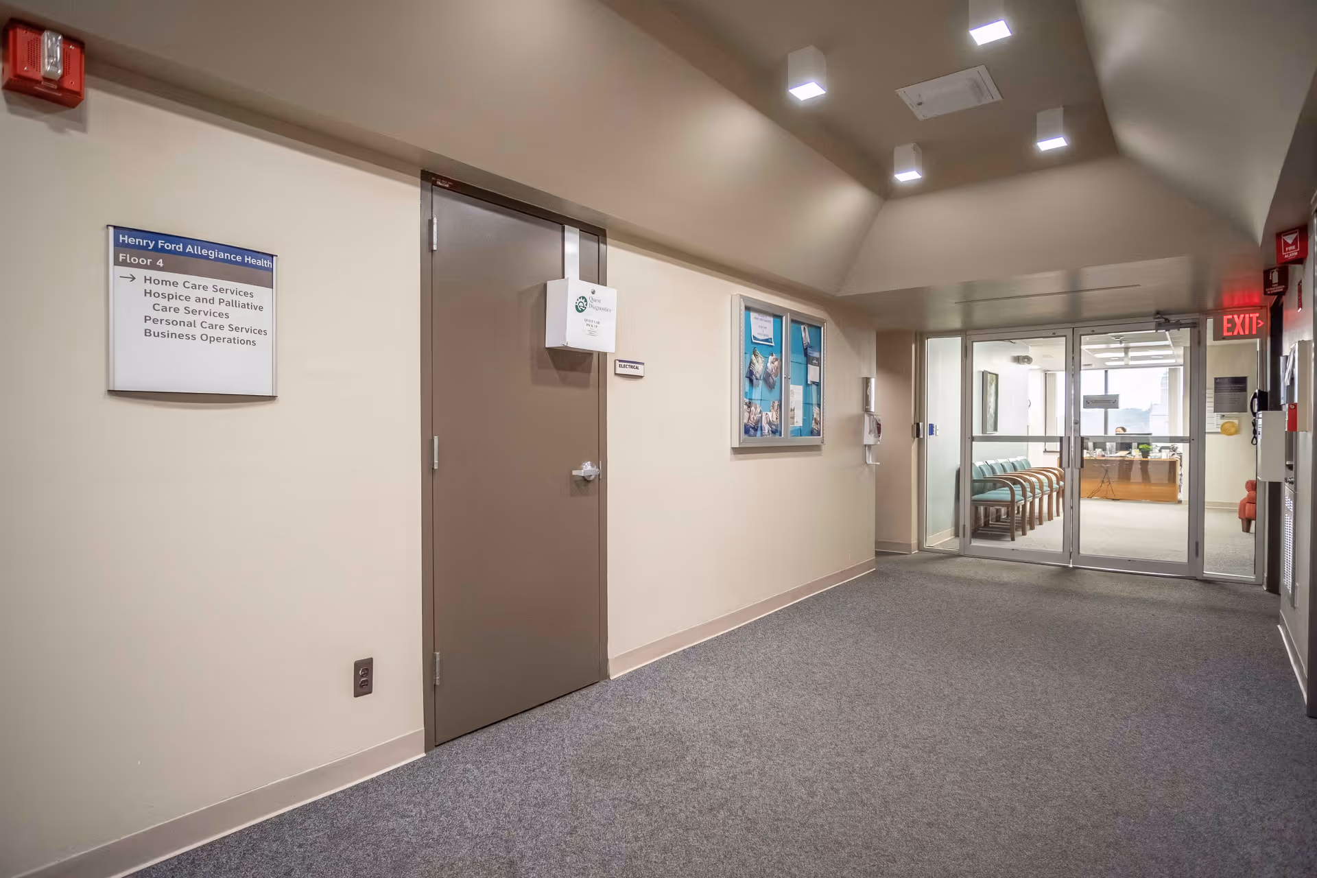 Interior hallway in a senior facility with doors, signs, and glass entry to a waiting area.