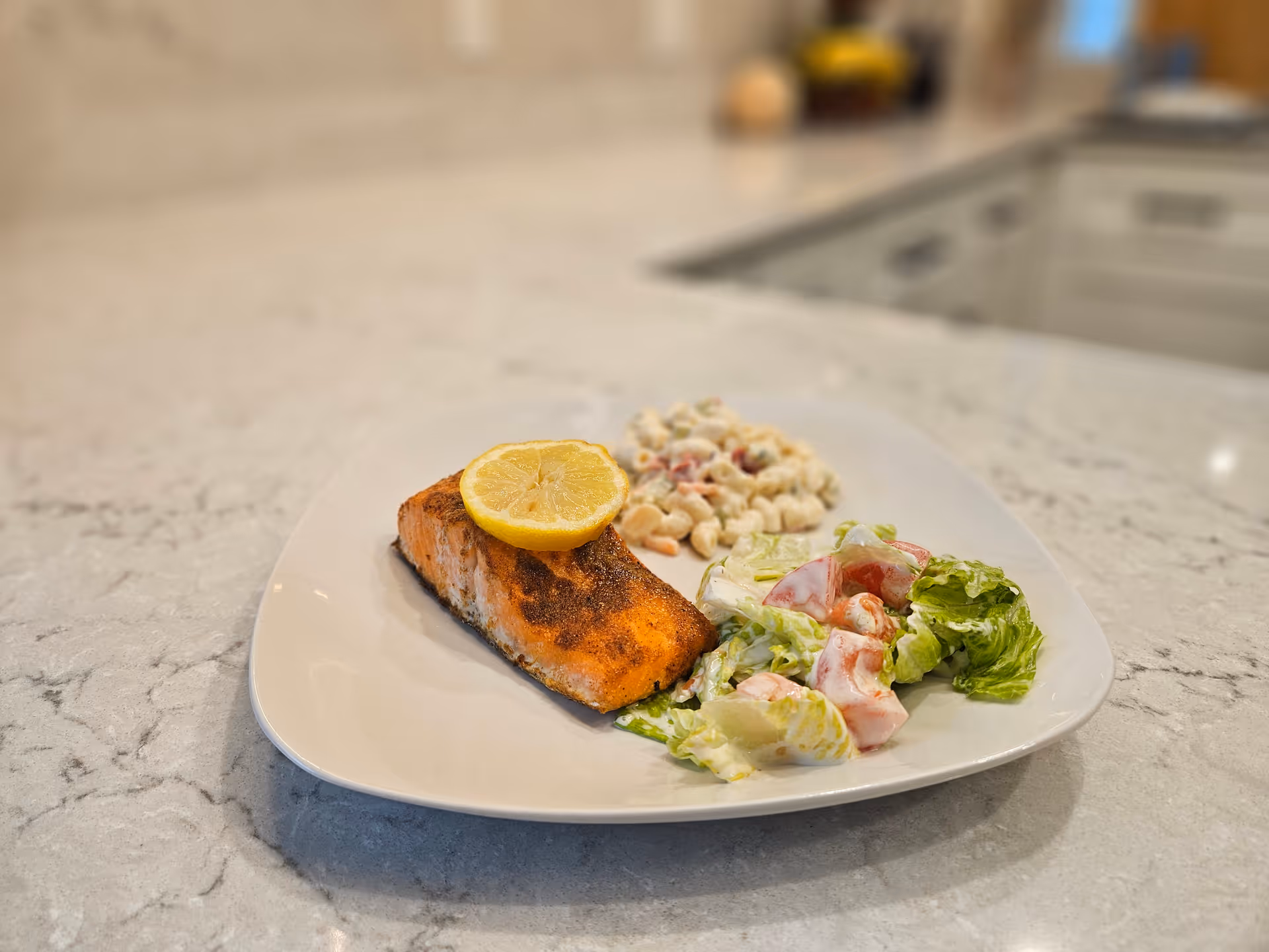 Plate with salmon, pasta salad, and greens on a marble kitchen counter.