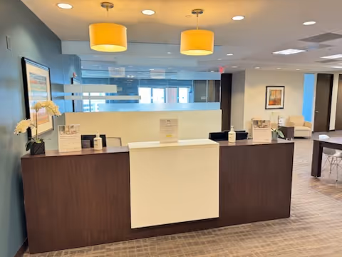 Reception desk in a modern lobby with teal walls and hanging yellow lights.