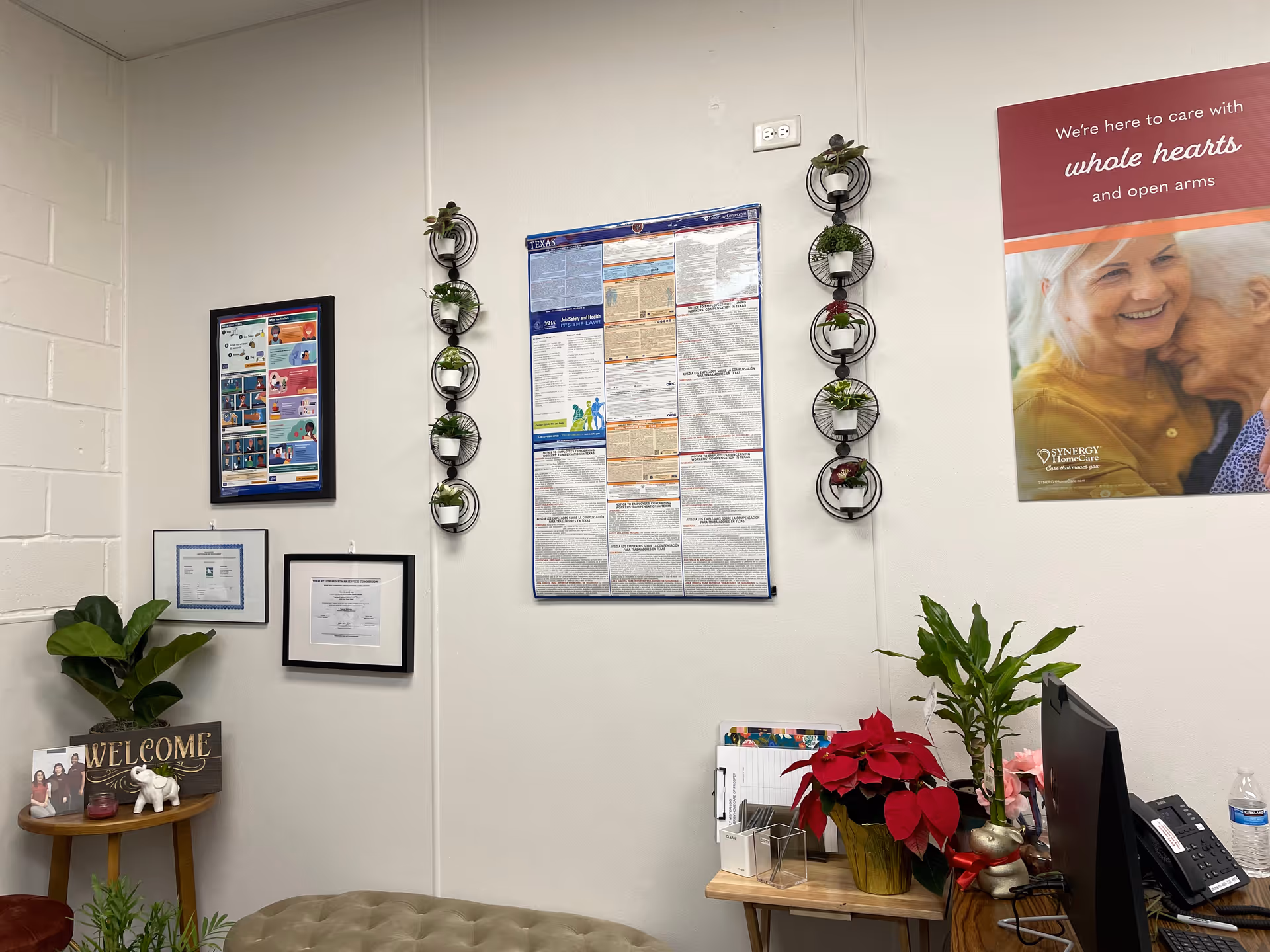 Indoor facility lobby with wall posters, decorative plants, a welcome sign, and a desk.