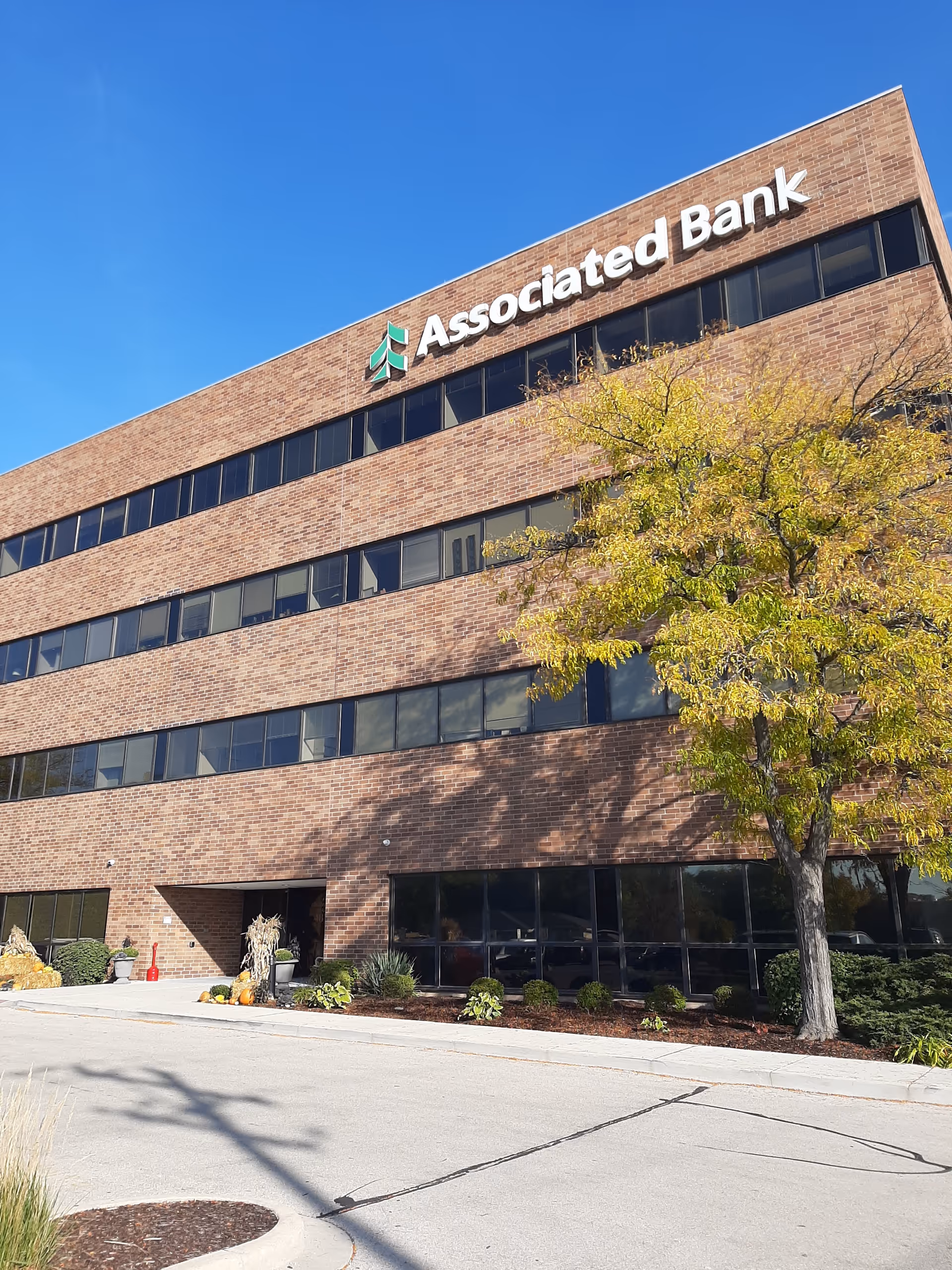 Brick office building with a large Associated Bank sign and trees nearby