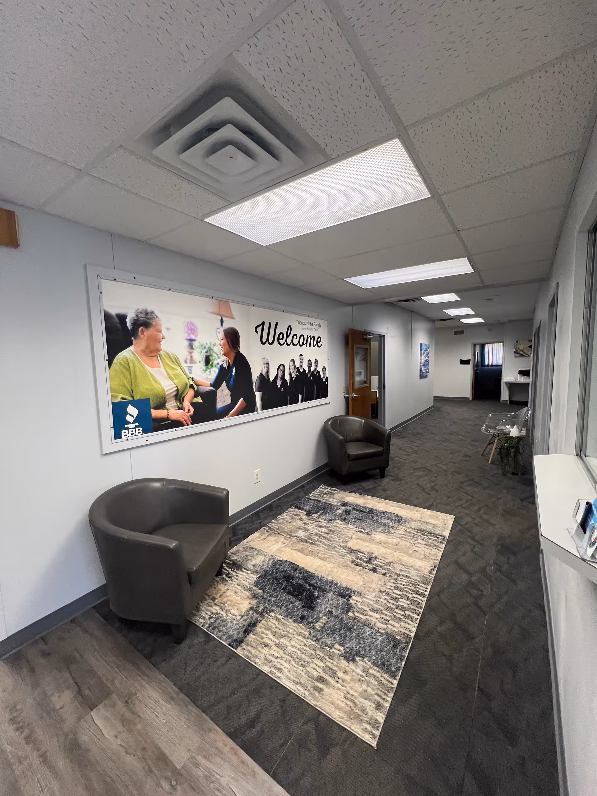 Interior lobby hallway with two gray chairs, a Welcome banner, and a rug.