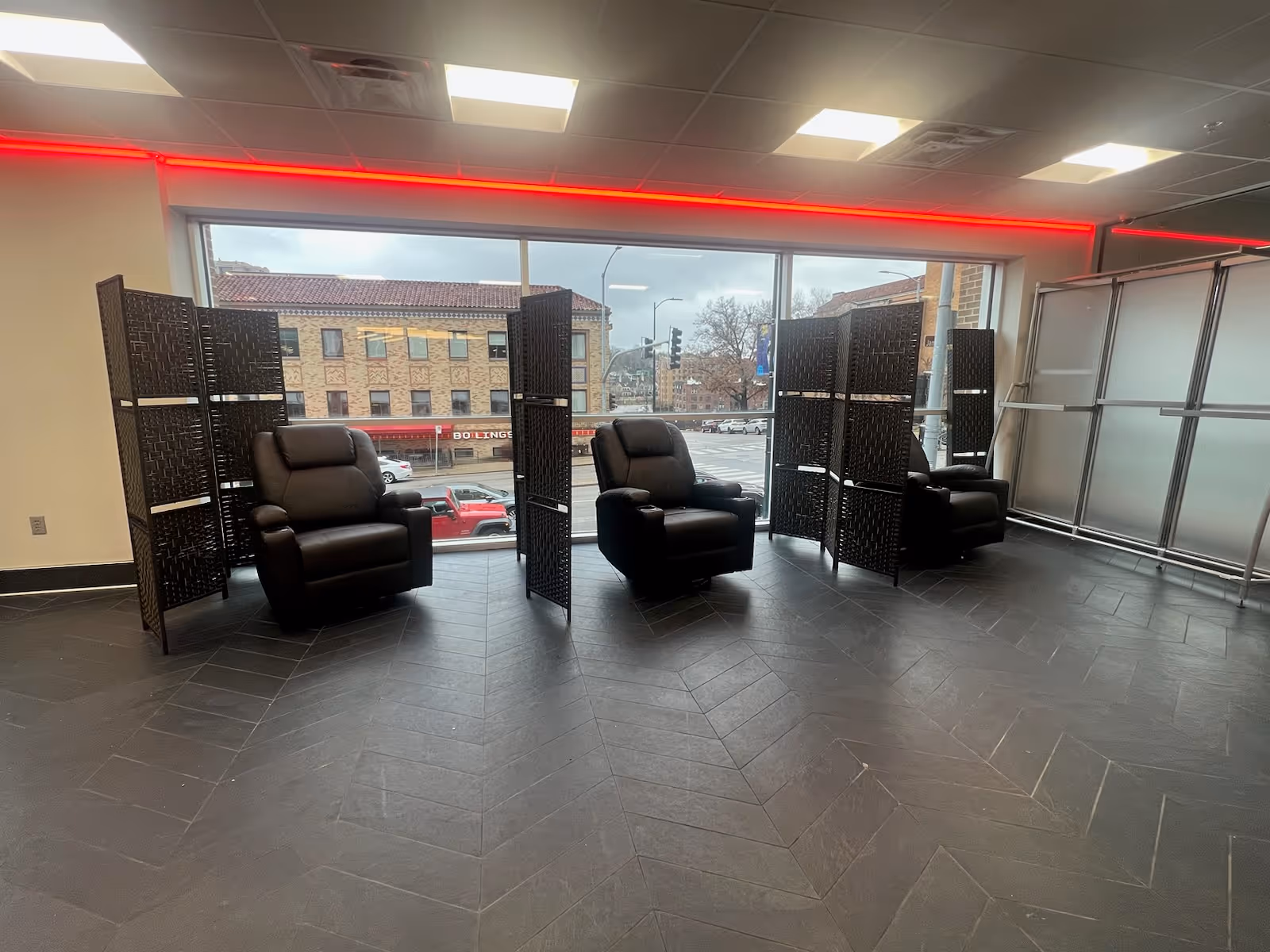 Lobby seating area with three black leather recliners and privacy screens by windows.