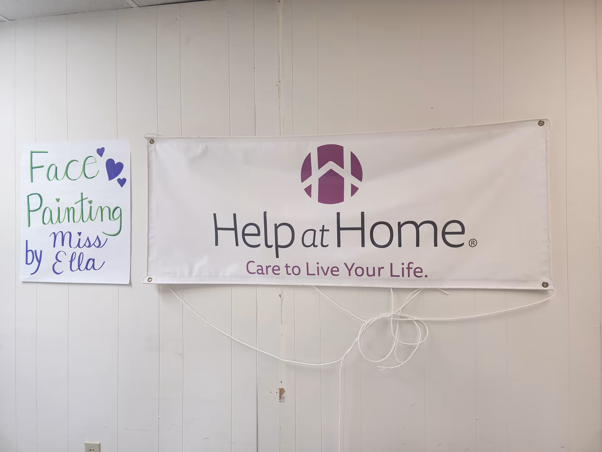Interior wall with Help at Home banner and a face painting sign