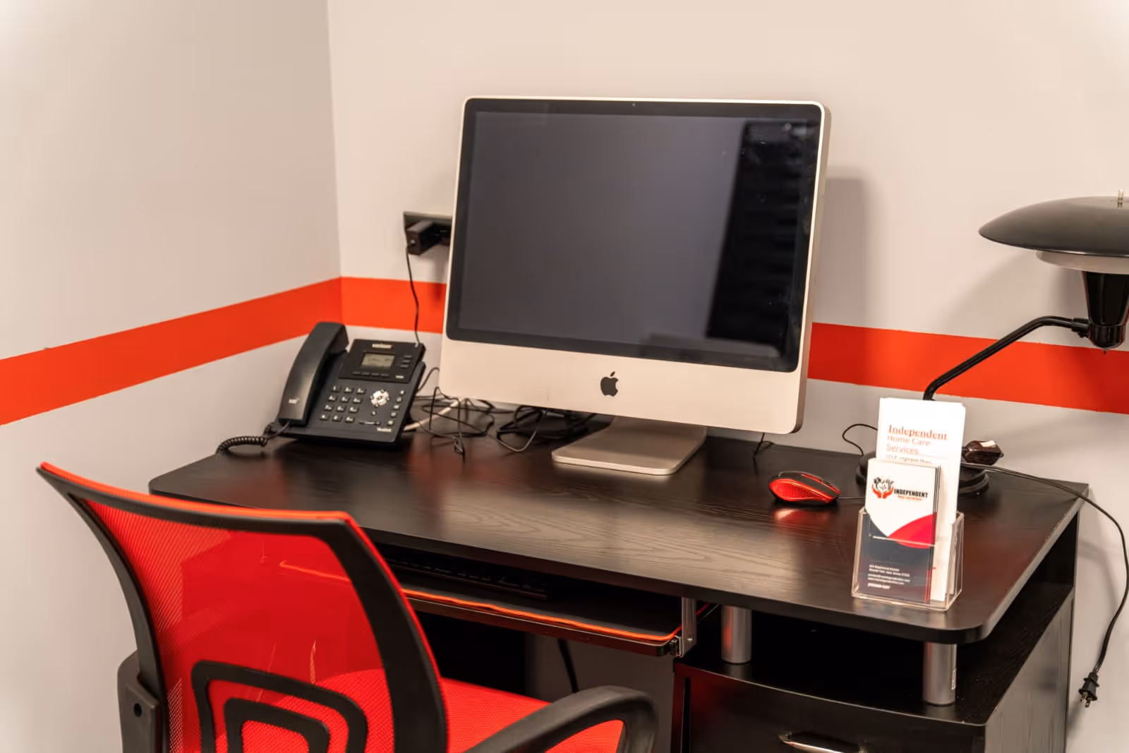 Interior desk setup with an iMac, phone, and red chair in a facility.