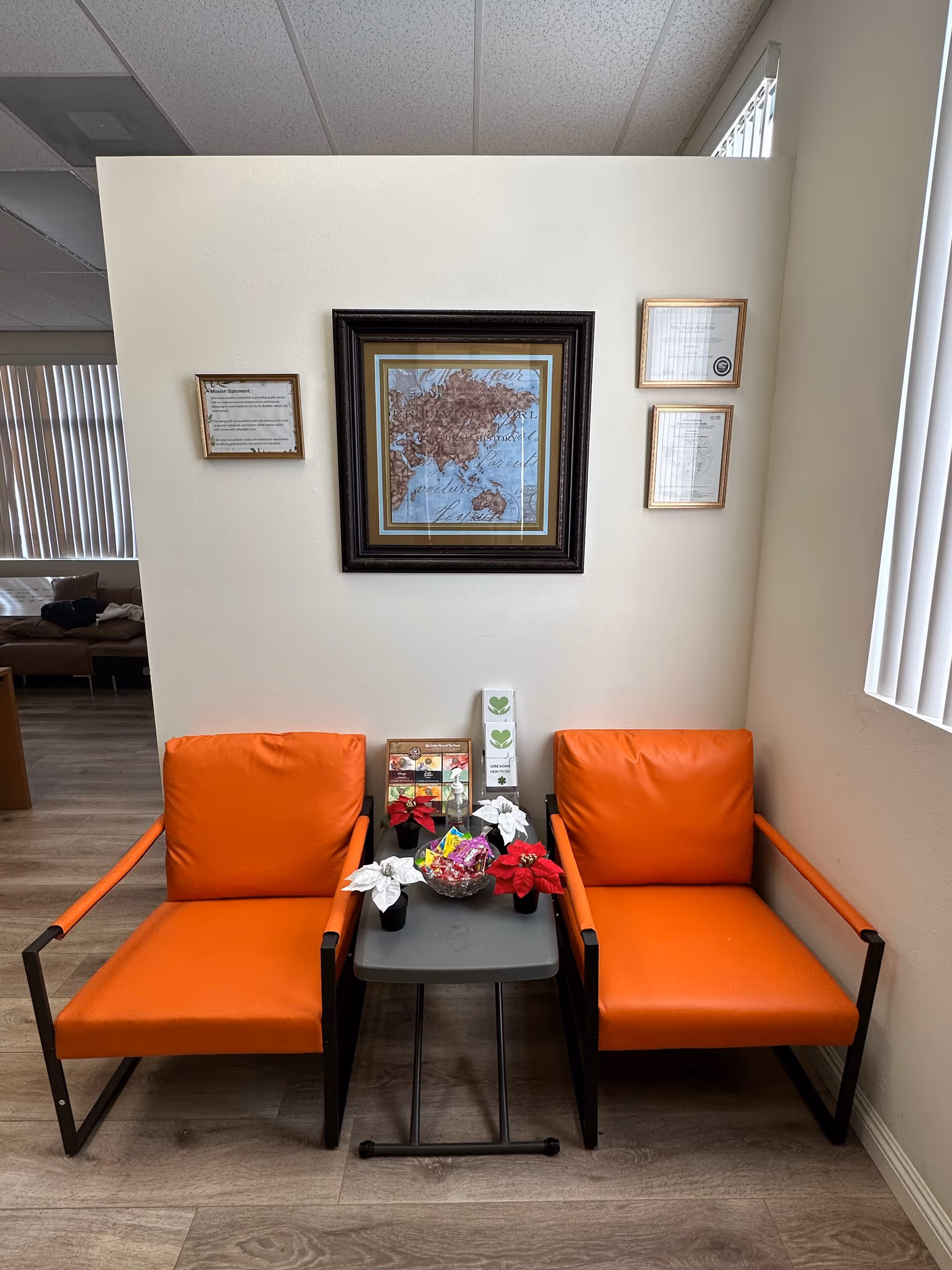 Two orange armchairs with a small table between, framed art on a beige wall.