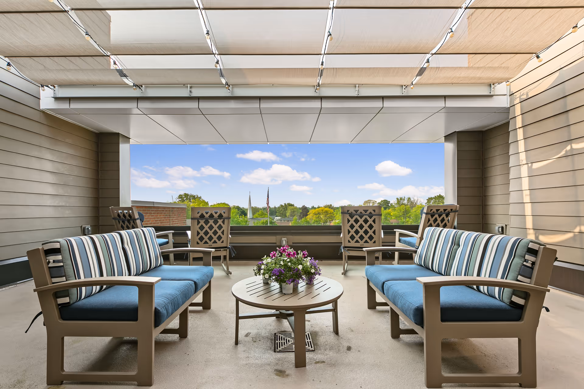 Outdoor patio with blue-cushioned seating, central table, and flower arrangement.