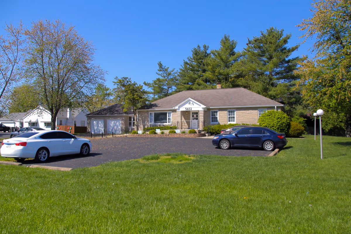 Single-story brick senior living facility with a front entrance, parking lot, and green lawn.