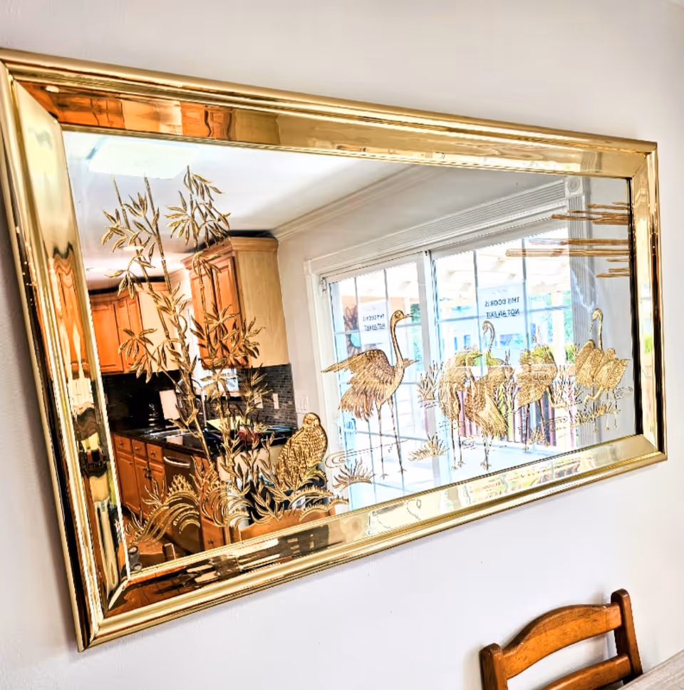 A gold-framed mirror reflects a kitchen with wooden cabinets and bamboo decor.
