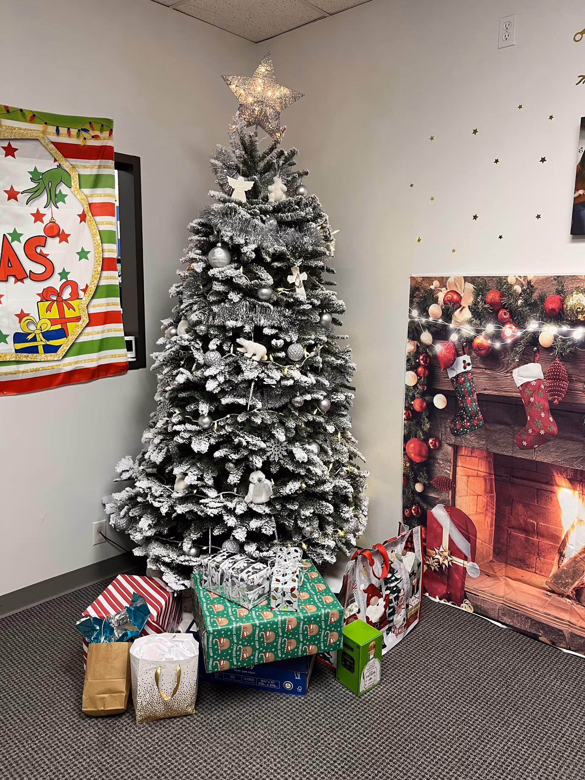 Snow-dusted Christmas tree with wrapped gifts in a senior facility common area.