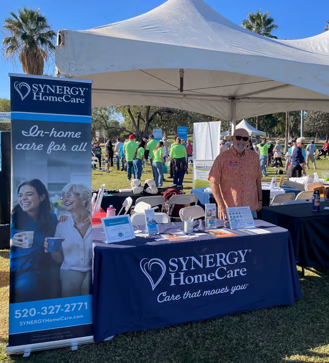 Outdoor Synergy HomeCare booth with staff, banners, and informational materials under a tent.