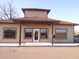 Front view of a single-story beige brick building with glass entry door.