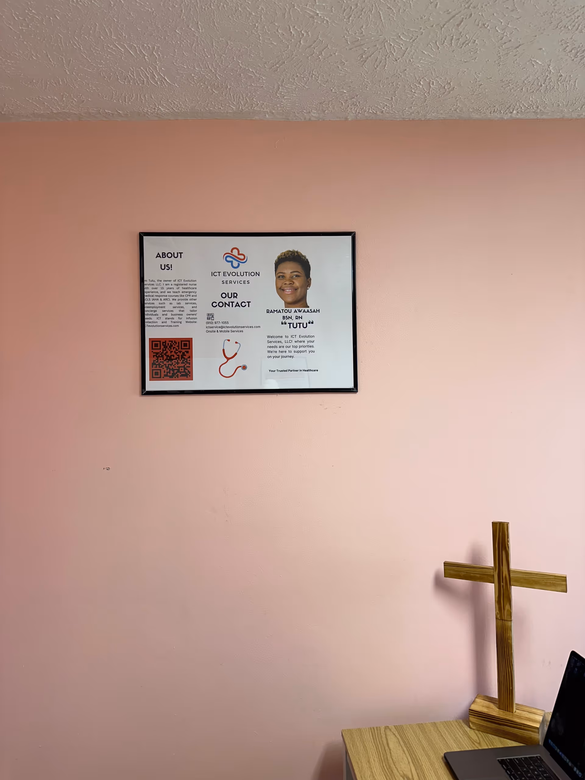 Interior pink wall with framed ICT Evolution Services poster and a wooden cross on a desk