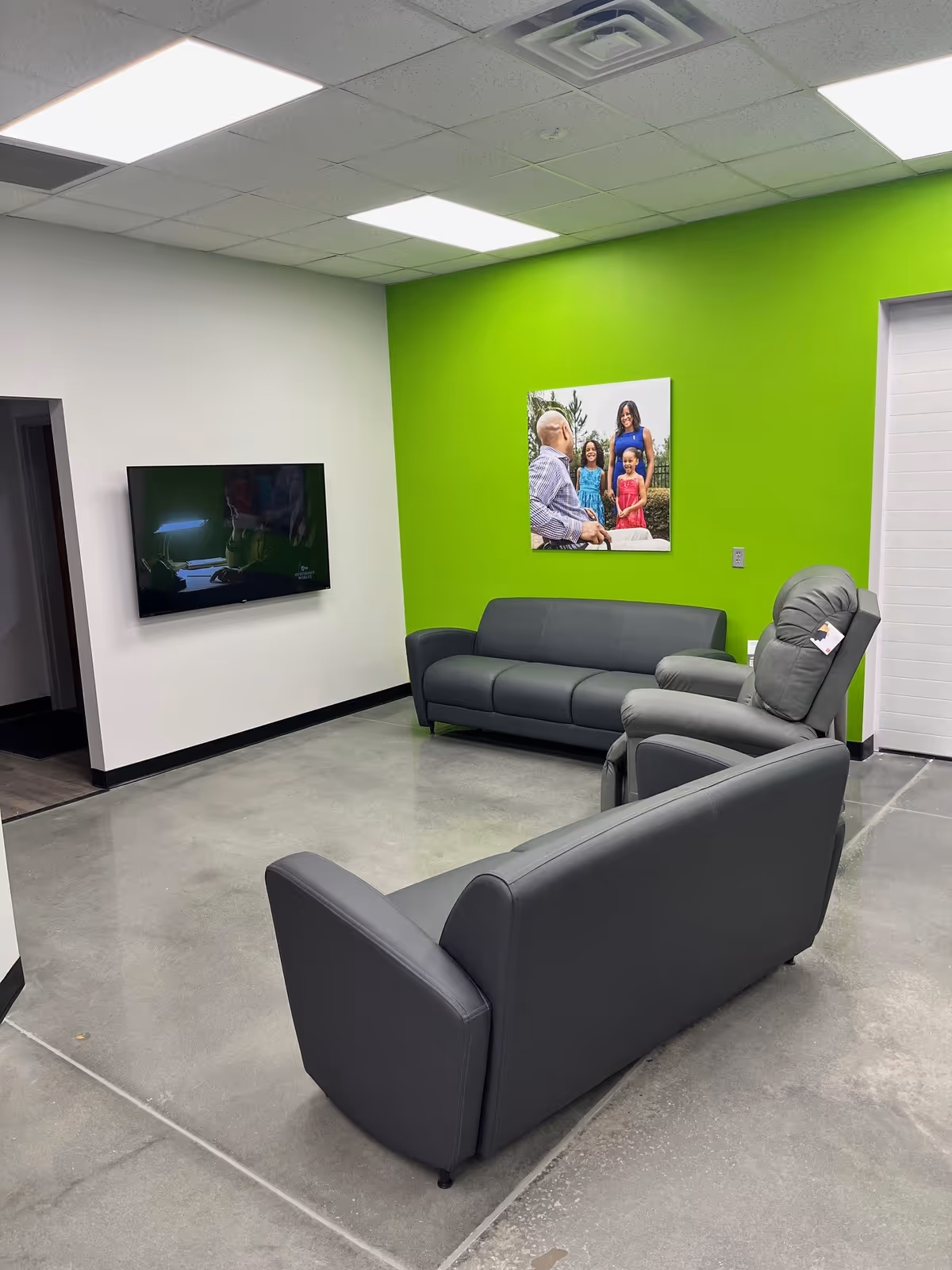 Modern lounge area with gray couches, a wall-mounted TV, and a bright green accent wall.