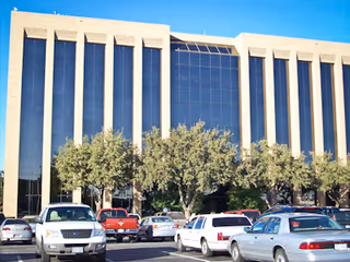 Exterior view of a modern building with glass windows and a parking lot.