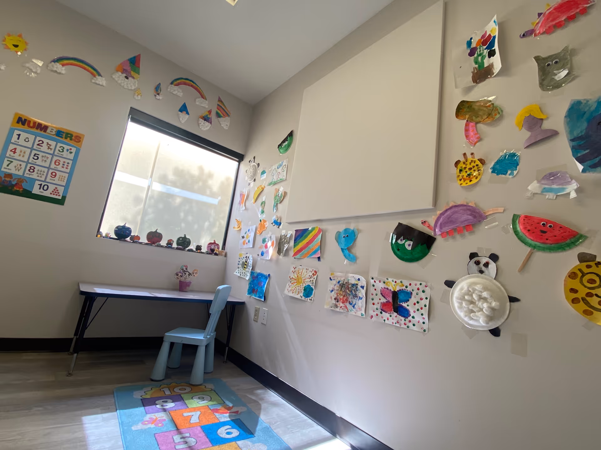 A bright interior room with a small table and chair, walls covered in children's art.