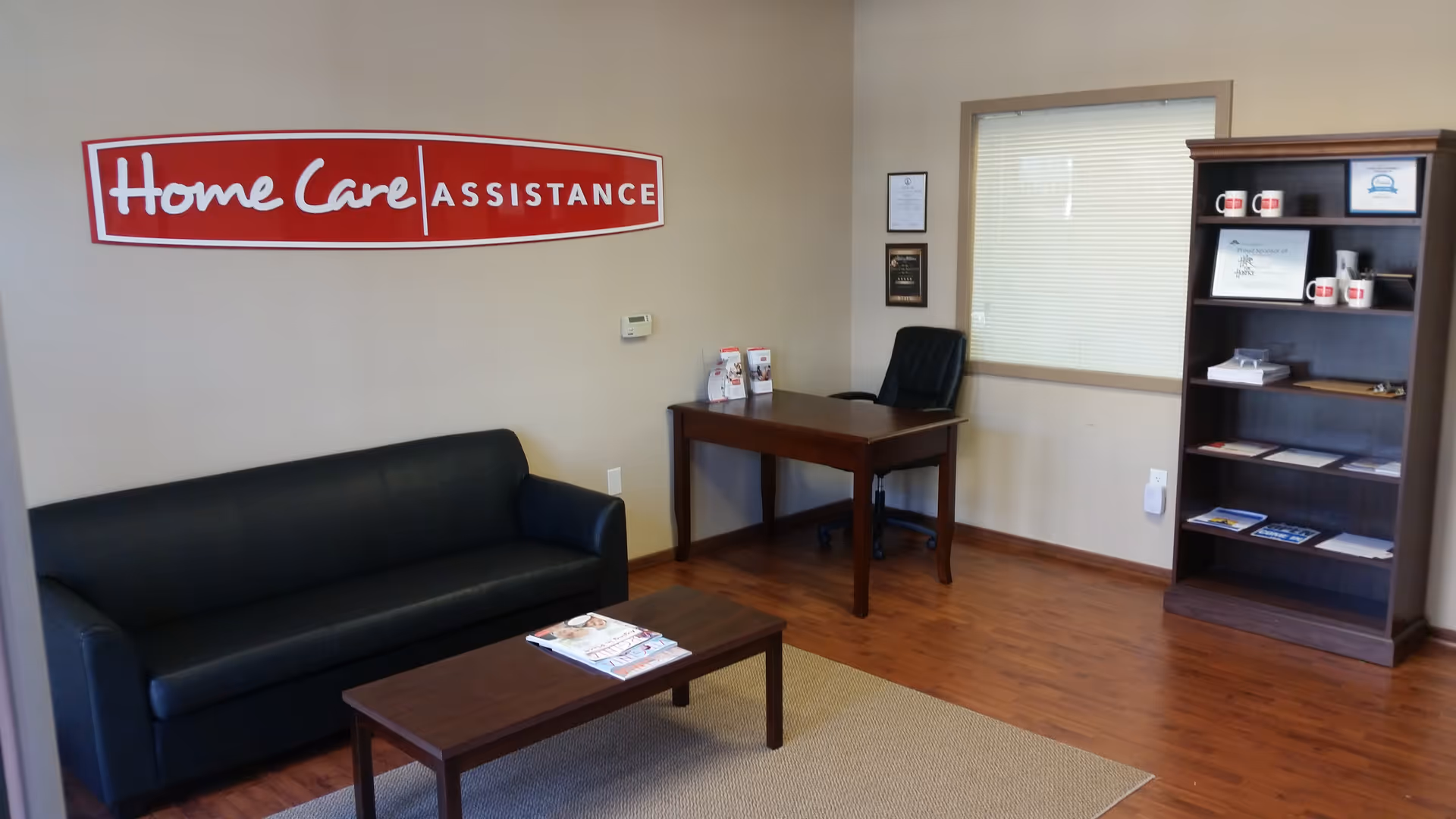 Lobby-style office space with sofa, desk, bookshelf, and a Home Care Assistance sign.