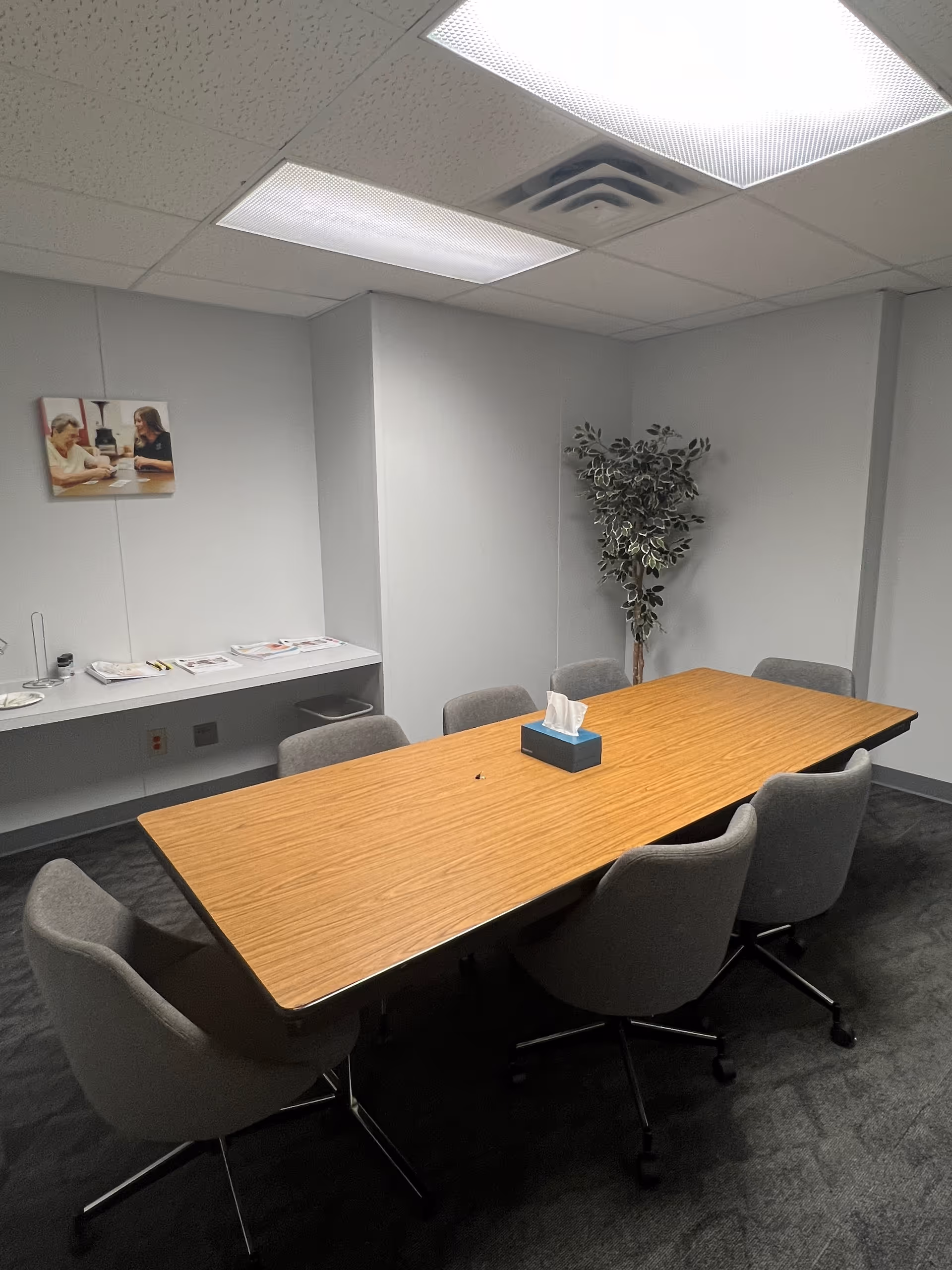 Rectangular wooden table surrounded by gray chairs in a plain interior meeting room.