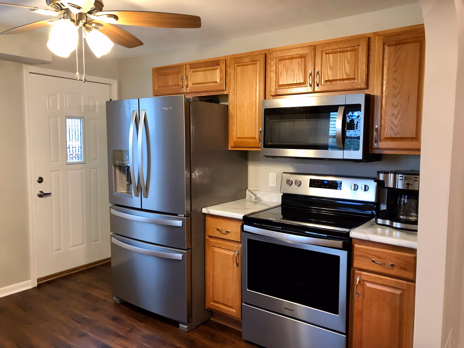 Modern kitchen with stainless steel appliances, wooden cabinets, and a ceiling fan.