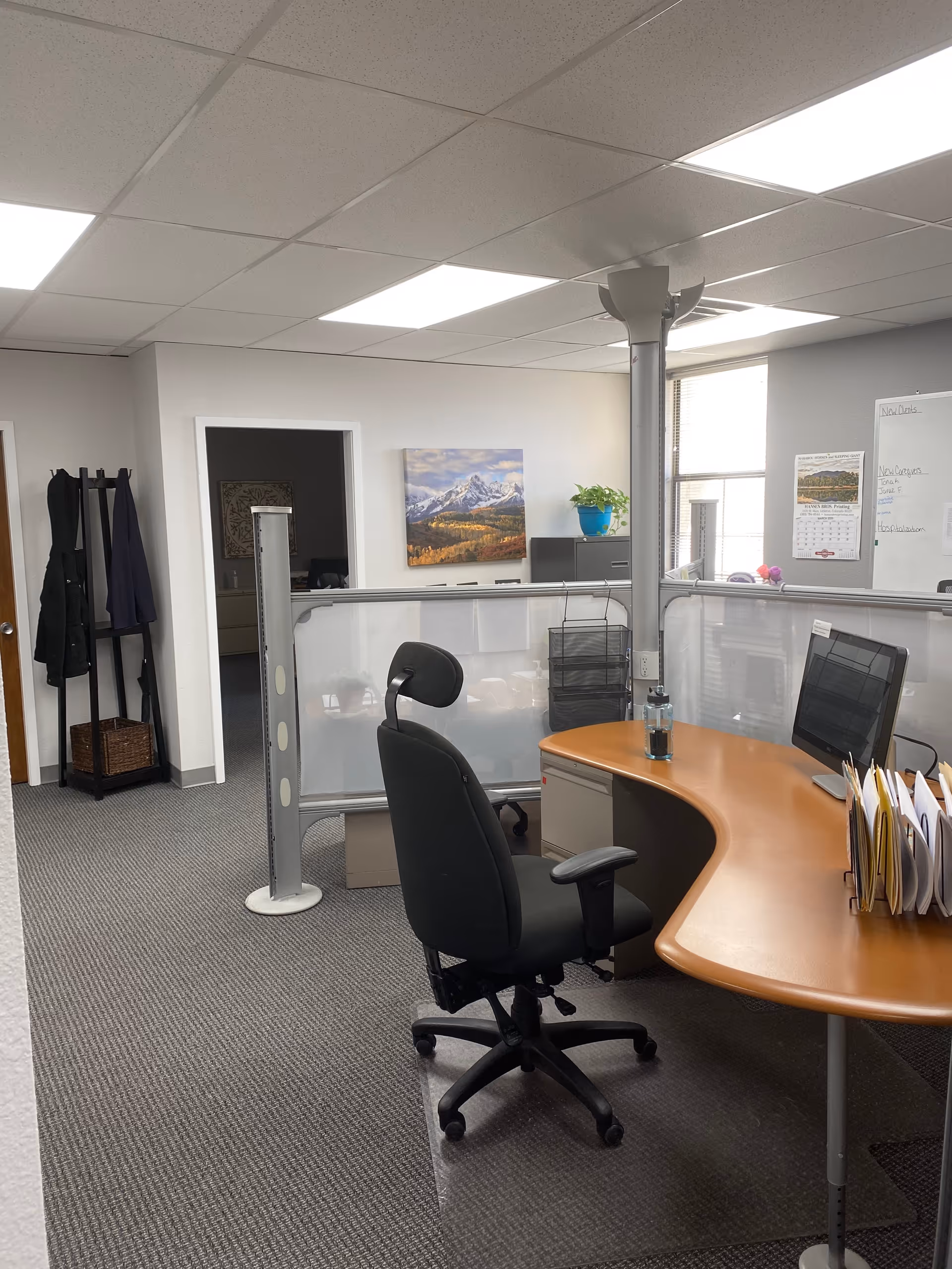 Interior reception area with curved wooden desk, computer, office chair, coats, and mountain artwork.