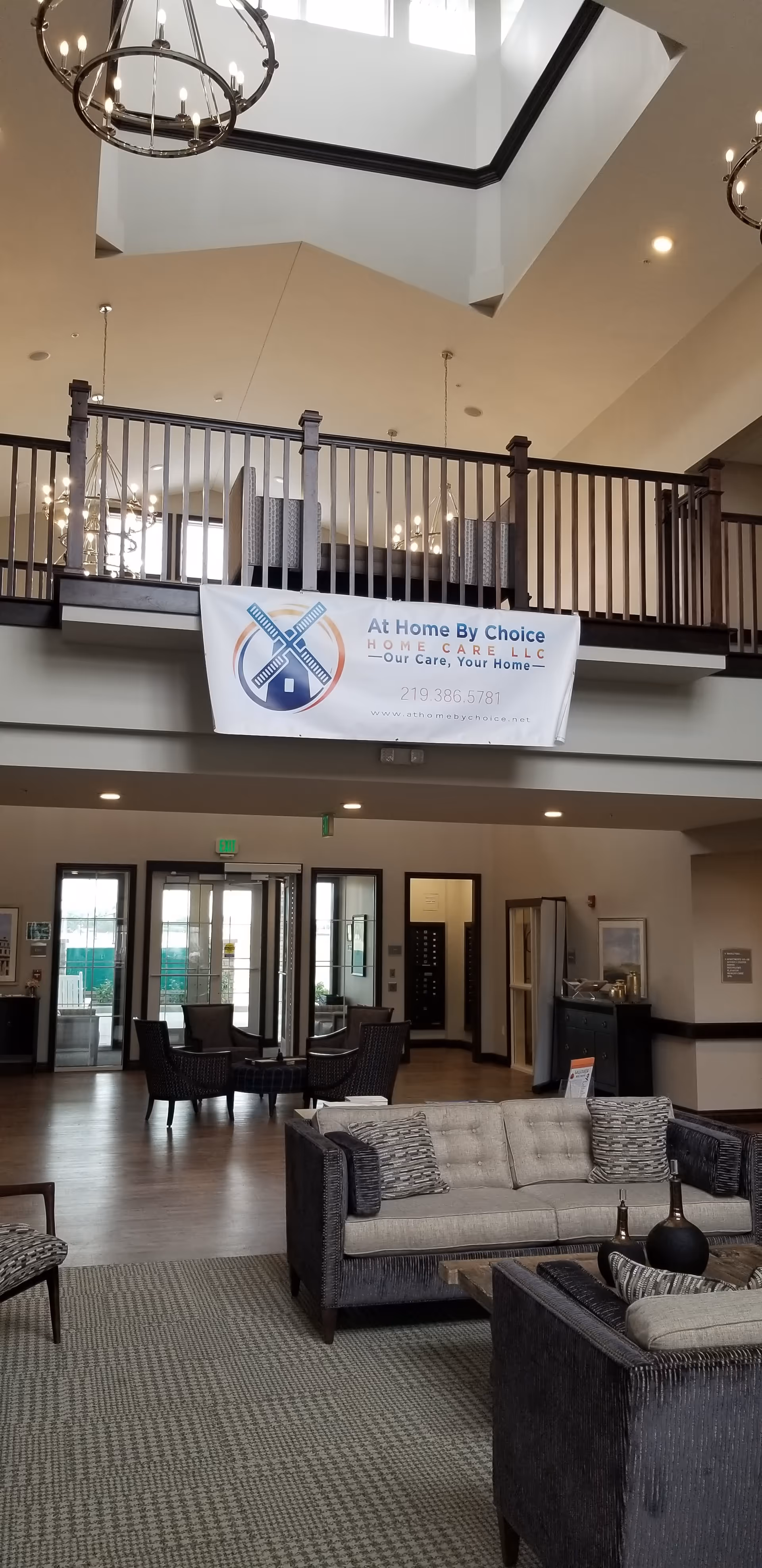 Spacious lobby area with seating, a second-floor balcony, and a banner for At Home By Choice.